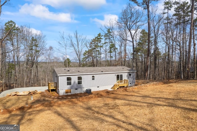 exterior space featuring dirt driveway, a view of trees, crawl space, and central air condition unit