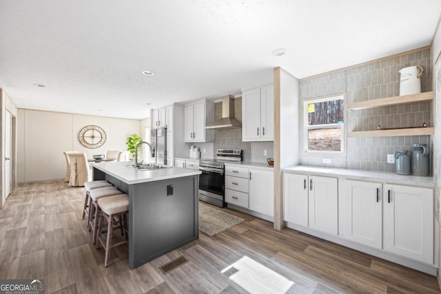 kitchen featuring stainless steel appliances, decorative backsplash, light wood-style floors, a sink, and wall chimney exhaust hood