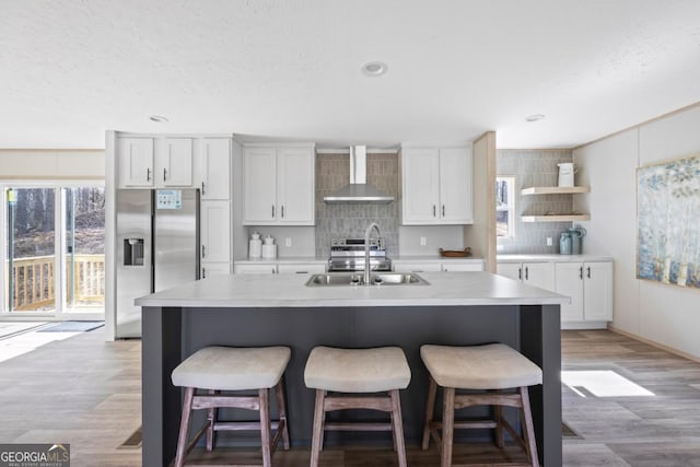 kitchen featuring wall chimney exhaust hood, appliances with stainless steel finishes, white cabinets, and a sink