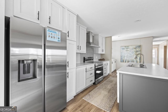 kitchen with light wood finished floors, appliances with stainless steel finishes, light countertops, wall chimney range hood, and a sink