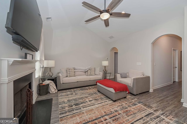 living area with arched walkways, a fireplace, wood finished floors, visible vents, and vaulted ceiling