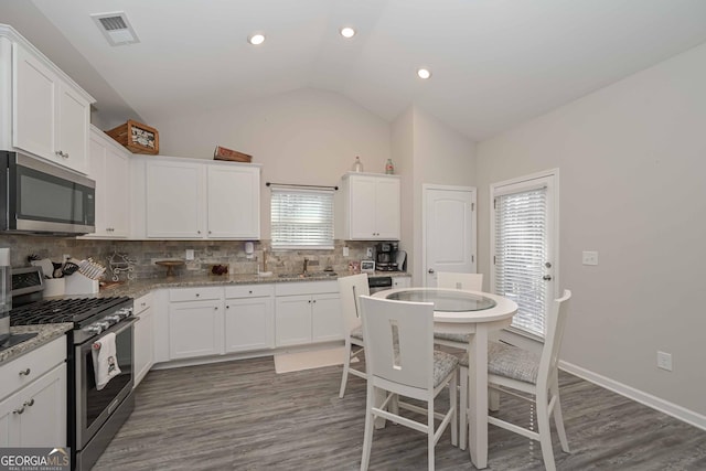 kitchen with visible vents, white cabinets, vaulted ceiling, stainless steel appliances, and a sink