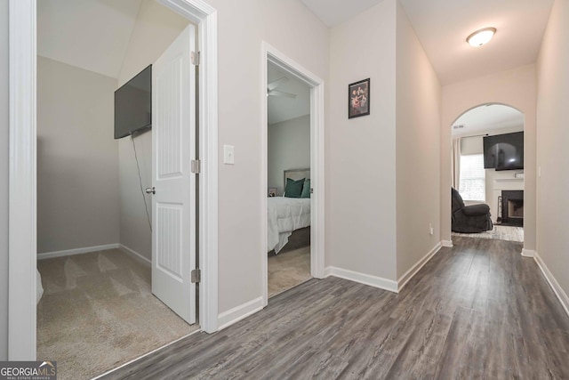 hall featuring baseboards, arched walkways, and wood finished floors