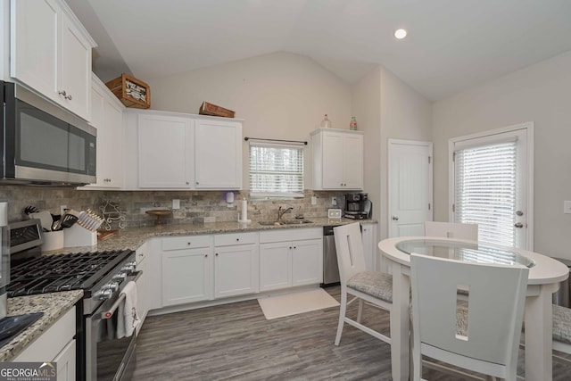 kitchen featuring stainless steel appliances, white cabinetry, vaulted ceiling, and a sink