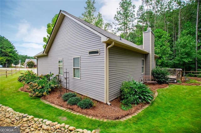 view of side of property with a deck, a yard, and a chimney