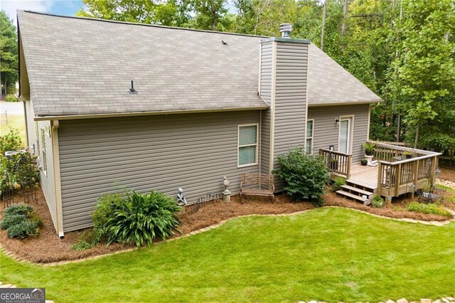 back of property with a chimney, a deck, and a yard