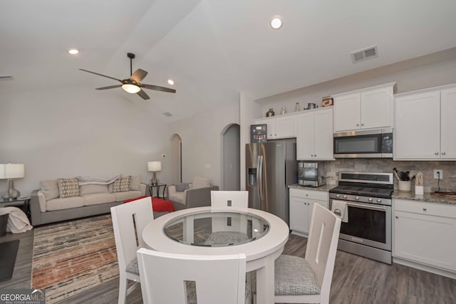 kitchen featuring arched walkways, visible vents, appliances with stainless steel finishes, white cabinetry, and vaulted ceiling