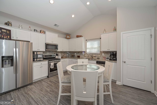 kitchen featuring lofted ceiling, visible vents, appliances with stainless steel finishes, white cabinets, and wood finished floors