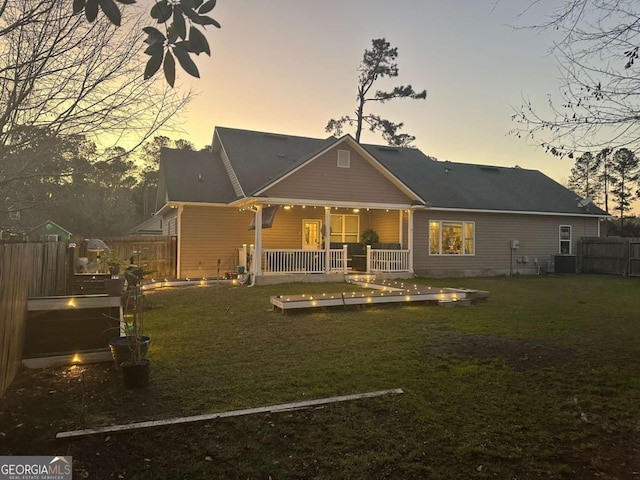 back of house at dusk featuring central AC unit, a lawn, and fence