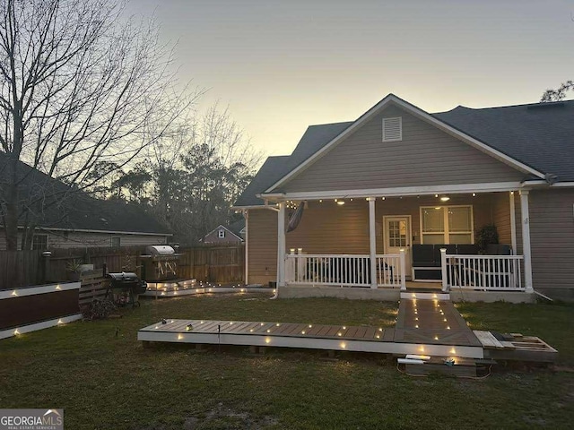 back of property at dusk with a porch, a lawn, and fence