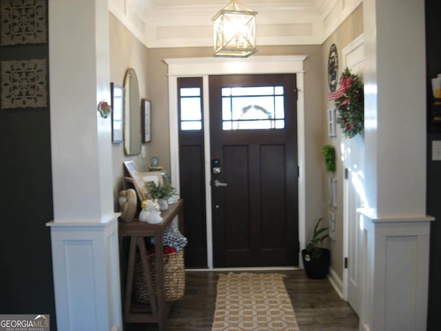 foyer entrance with a decorative wall, wainscoting, dark wood finished floors, and crown molding