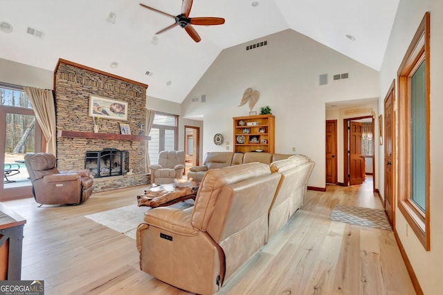 living area featuring high vaulted ceiling, light wood-type flooring, visible vents, and a fireplace