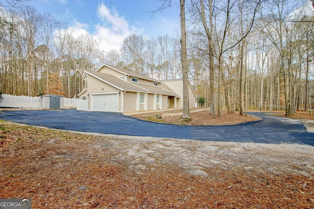 view of front of property featuring a garage, aphalt driveway, an outbuilding, a storage unit, and fence