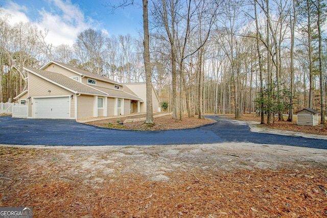 view of home's exterior featuring aphalt driveway, a garage, a storage shed, an outdoor structure, and fence