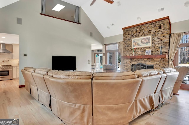 living room featuring light wood-type flooring, visible vents, and a stone fireplace