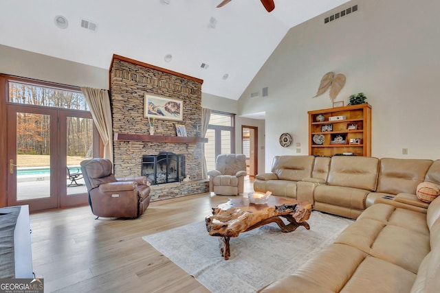 living room featuring high vaulted ceiling, a fireplace, visible vents, and wood finished floors