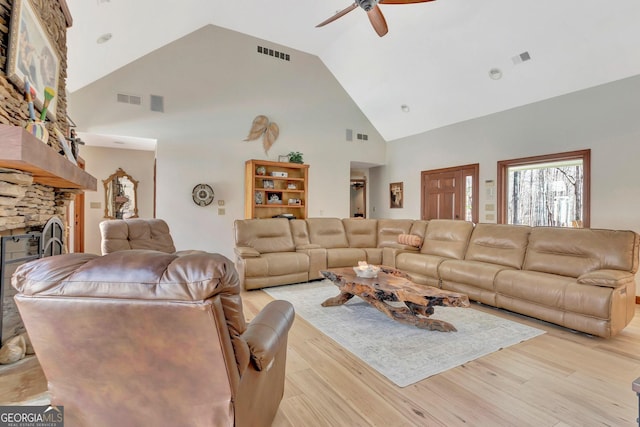 living room with a stone fireplace, light wood-style flooring, high vaulted ceiling, and visible vents