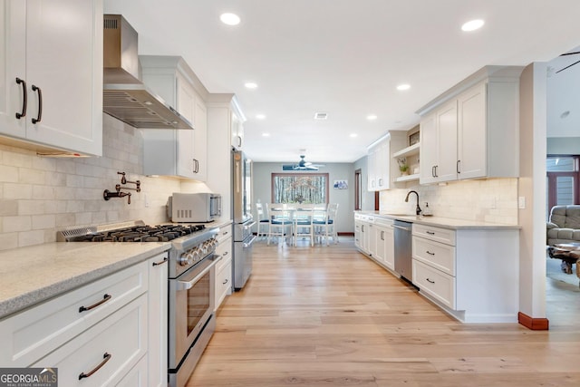 kitchen with wall chimney exhaust hood, light wood-style flooring, appliances with stainless steel finishes, white cabinetry, and open shelves