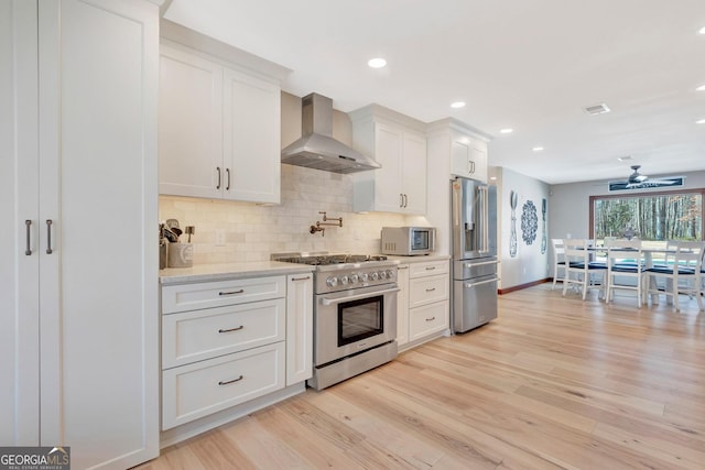 kitchen featuring light wood-style flooring, white cabinetry, wall chimney exhaust hood, tasteful backsplash, and high end appliances