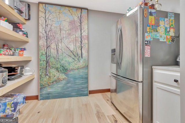 kitchen featuring light wood-style flooring, light countertops, stainless steel refrigerator with ice dispenser, and baseboards