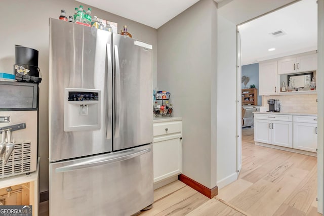 kitchen with tasteful backsplash, light countertops, white cabinetry, light wood-type flooring, and stainless steel fridge