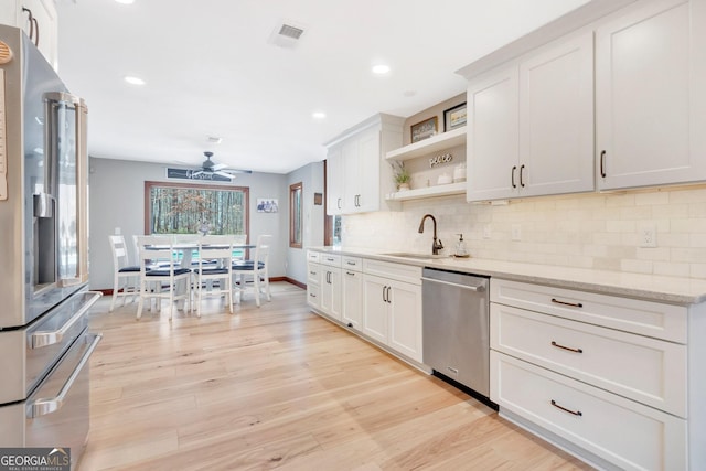 kitchen with light wood finished floors, open shelves, decorative backsplash, appliances with stainless steel finishes, and a sink