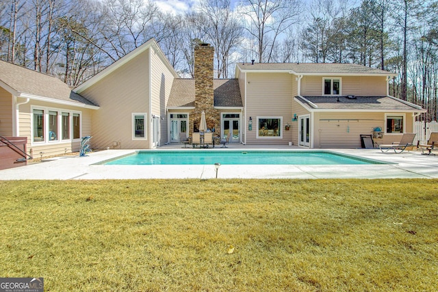 back of house featuring a chimney, a lawn, a patio area, and an outdoor pool