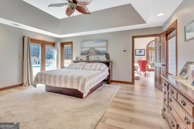 bedroom featuring baseboards, visible vents, access to outside, a tray ceiling, and light wood-type flooring