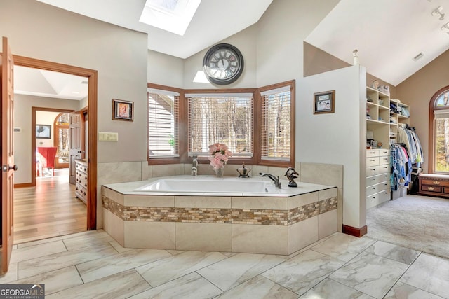 bathroom with high vaulted ceiling, a skylight, marble finish floor, a spacious closet, and a bath