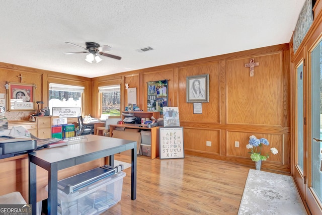 interior space featuring a ceiling fan, light wood-type flooring, visible vents, and a textured ceiling