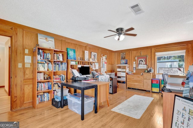 office featuring a textured ceiling, ceiling fan, wood walls, wood finished floors, and visible vents