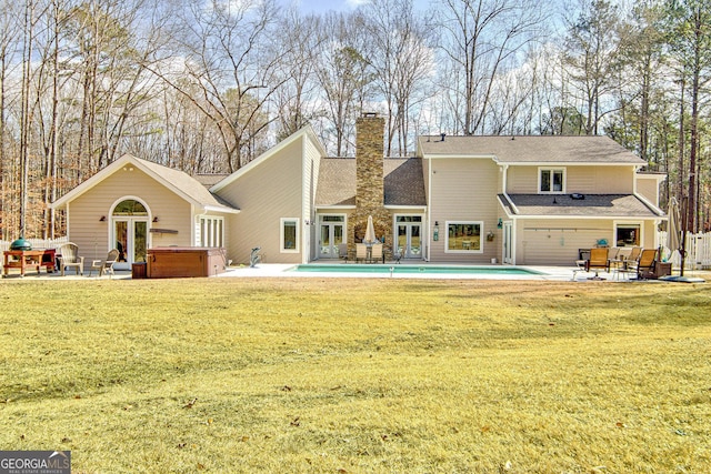 rear view of house featuring a yard, a chimney, a patio, a hot tub, and an outdoor pool