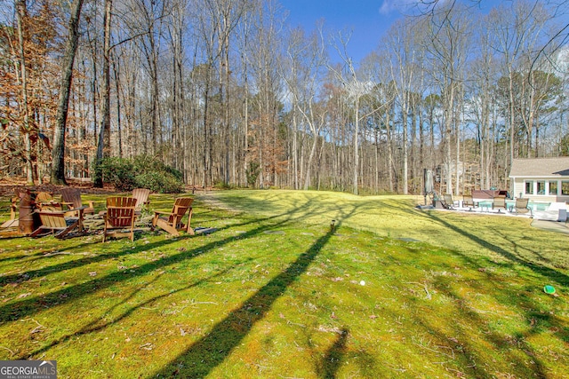 view of yard featuring an outdoor fire pit, a patio area, an outdoor pool, and a forest view