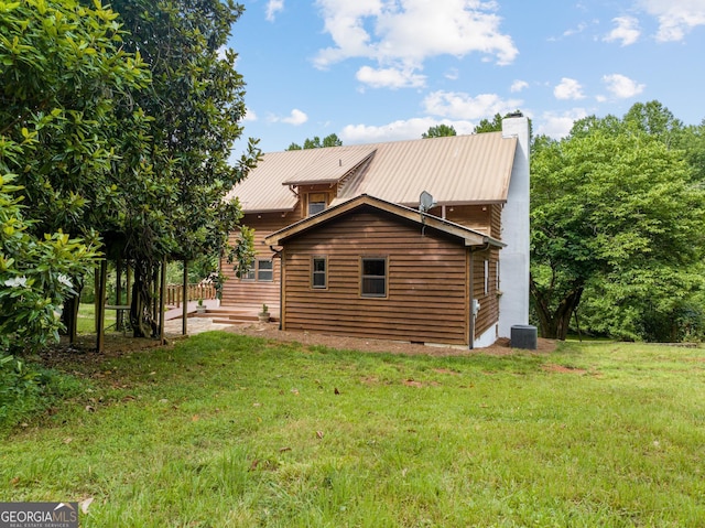 rear view of property featuring metal roof, a yard, a chimney, and central air condition unit