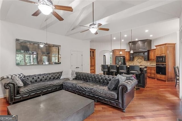 living room featuring arched walkways, ceiling fan, high vaulted ceiling, light wood-style floors, and beam ceiling