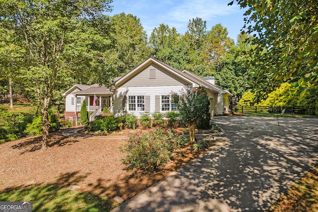 view of front facade featuring driveway, covered porch, a chimney, and fence