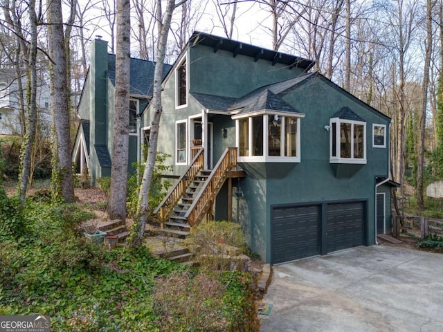 chalet / cabin with an attached garage, driveway, stairway, stucco siding, and a chimney