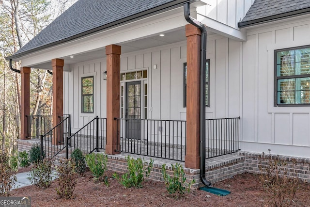 view of exterior entry with covered porch, roof with shingles, and board and batten siding