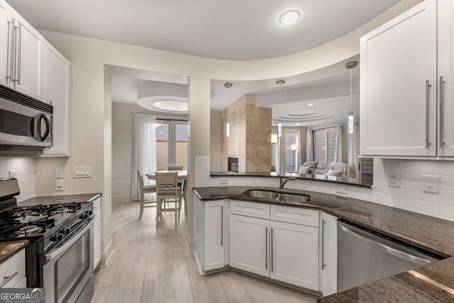 kitchen with a sink, appliances with stainless steel finishes, light wood-type flooring, tasteful backsplash, and dark stone countertops