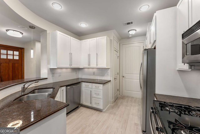 kitchen featuring visible vents, appliances with stainless steel finishes, a sink, dark stone counters, and white cabinetry