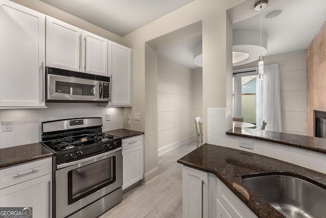 kitchen with light wood-type flooring, dark stone countertops, white cabinets, and stainless steel appliances