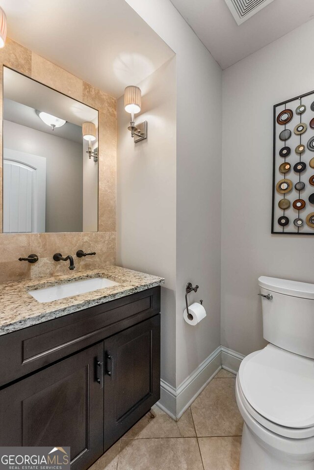 half bath with baseboards, tile patterned flooring, vanity, and toilet