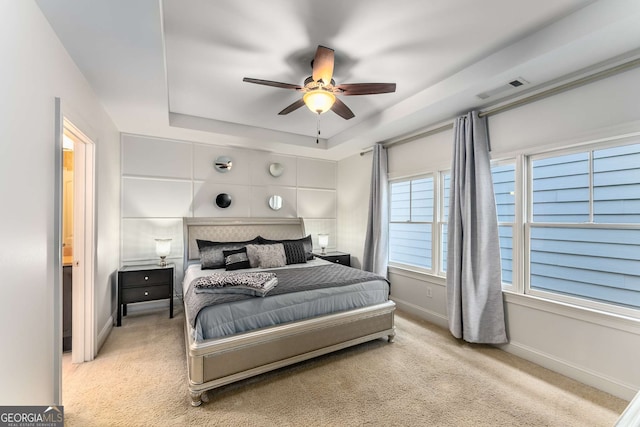 carpeted bedroom with a ceiling fan, visible vents, a tray ceiling, and baseboards