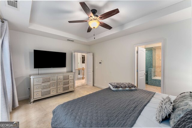 bedroom with visible vents, light carpet, baseboards, a tray ceiling, and ensuite bath