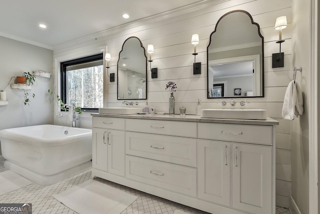 full bath featuring ornamental molding, a freestanding tub, a sink, and double vanity