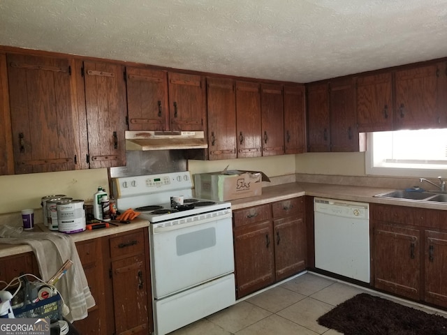 kitchen featuring white appliances, under cabinet range hood, light countertops, and a sink