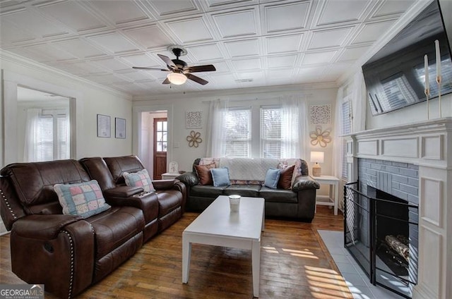 living area featuring ceiling fan, a fireplace, wood finished floors, ornamental molding, and an ornate ceiling