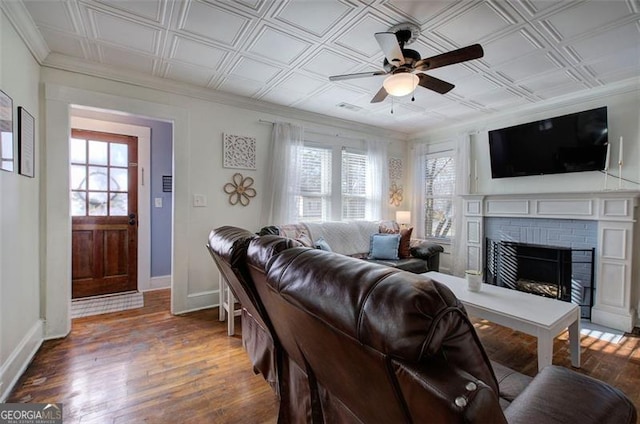 living room with an ornate ceiling, wood-type flooring, a brick fireplace, a healthy amount of sunlight, and baseboards