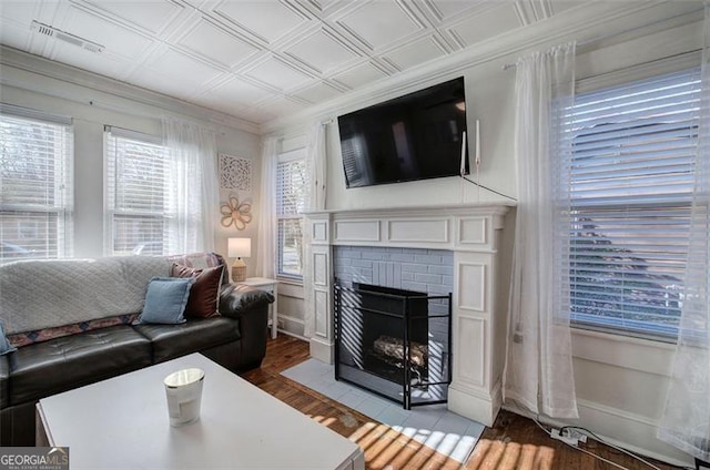 living room with an ornate ceiling, crown molding, visible vents, a brick fireplace, and wood finished floors