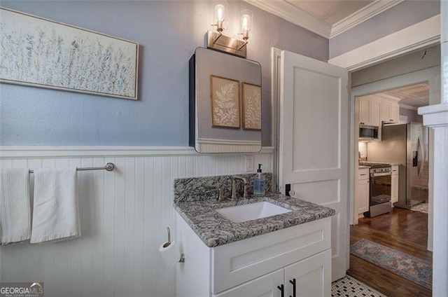 bathroom with a wainscoted wall, wood finished floors, crown molding, and vanity